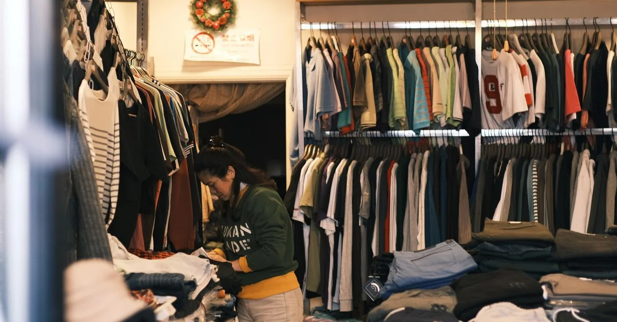 Una mujer organizando ropa en una acogedora boutique de ropa con una amplia selección en exhibición.