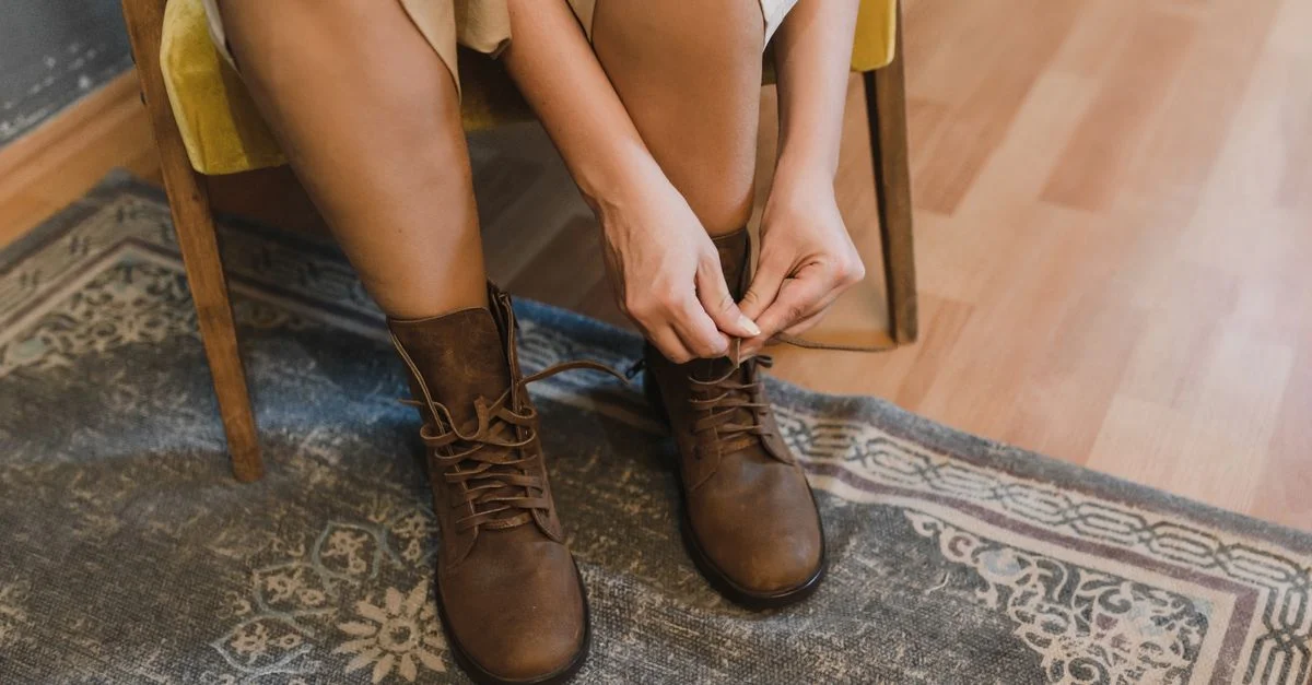 Una mujer atando botas de cuero marrón mientras está sentada en una silla, sobre una alfombra estampada.
